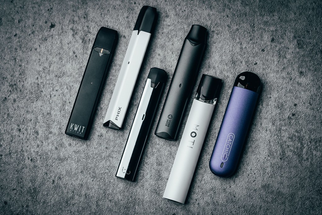 Assorted pod vape devices laid out on a gray stone surface